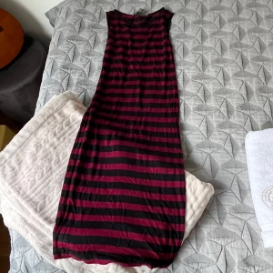 Svart och vinröd långklänning - Säljer en långklänning med breda svarta och vinröda ränder. Klänningen är ärmlös och har en rak, avslappnad passform som känns chill och enkel att bära. Perfekt för dig som gillar en lite edgy stil med tydliga kontraster.