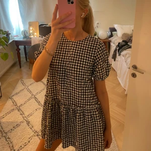 Svartvit rutig kort klänning - Supersöt kort klänning med svartvitt rutigt mönster och puffiga kortärmar. Klänningen har en rund halsringning och en volangkant nedtill som ger en chill och trendig vibe. Perfekt för dig som gillar en lekfull och avslappnad stil. 🩷🩷🩷 Skriv för fler bilder eller vid frågor. Pris kan diskuteras!😊😊