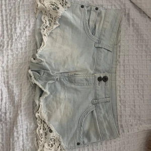 Ljusblå jeansshorts med spets - Supersnygga ljusblå jeansshorts med vita virkade spetsdetaljer längs kanterna. Storlek 38 men skulle säga att de är ganska små i storleken