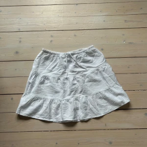 Vit Basic volang Kjol - Supersöt vit kjol i storlek XXS men skulle säga att den även passar XS-M. Kjolen har volanger och en mjuk resår i midjan. Ett utmärkt basplagg för både vardag,  fest och för sommarens alla dagar. Använd någon enstaka gång. Går även att bära som en topp.