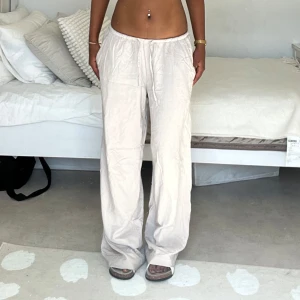 Beiga vida linnebyxor med snörning - Säljer ett par ljusbeiga linnebyxor med avslappnad passform och dragsko i midjan. Byxorna har breda ben och elastisk midja för extra komfort. Perfekta för en chill och stilren look under varmare dagar.