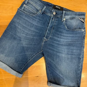 Blå jeansshorts från Replay, strl 32 - Snygga blå jeansshorts från Replay, modell RBJ 901 Short. Klassisk femficksdesign, uppvikta benslut och normal passform. Perfekta för sommaren och lätta att matcha med allt. Tidlös denim-look med Replay-logga på bakfickan.