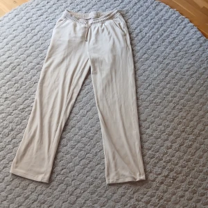 Beiga mjukisbyxor från Teen Studio - Snygga beiga mjukisbyxor från Teen Studio med elastisk midja och dragsko. Byxorna har raka ben, två fickor bak och är gjorda i mjukt material som känns skönt mot huden. Perfekta för chill dagar eller när du vill vara bekväm.