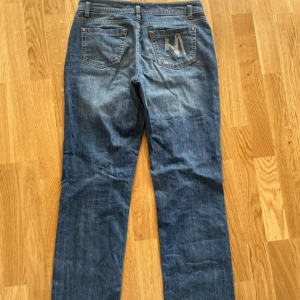 Blåa lågmidjade jeans med silver detaljer  - Blåa lågmidjade jeans med silver detaljer. Det står att dom är i strl 40 men skulle säga att dom är mer som strl 38. Bra skick, lite slitet på silverdetaljerna baktill.
