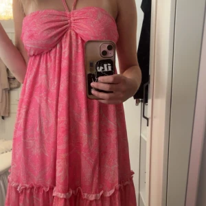 Rosa sommarklänning - Supersöt rosa kortklänning med halterneck och volangkant nertill. Klänningen har ett paisleymönster i ljusrosa och vitt, samt rynkdetalj vid bysten. Den är ärmlös och har öppen rygg, perfekt för varma dagar. Den är aldrig använd men den är väldigt fin. Dock passade den inte riktigt helt. Klänningen är från SHEIN, därav priset. Ord pris: 200