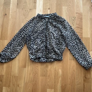 Leopardmönstrad jacka från Lindex Kids - Snygg leopardmönstrad jacka från Lindex Kids i storlek 134/140. Jackan har dragkedja framtill, resår i midjan och vid ärmslut samt lång ärm. Perfekt för dig som vill sticka ut med ett djurmönster och cool stil.den är väldigt tunn och genomskinlig