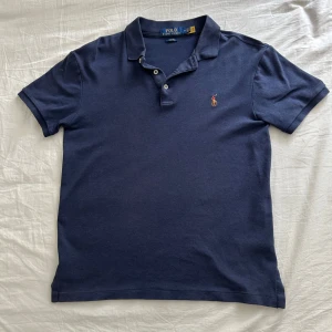 Marinblå Polo Ralph Lauren t-shirt - Snygg marinblå t-shirt från Polo Ralph Lauren i slim fit-modell. Klassisk pikékrage med två knappar och broderad polospelare på bröstet. Tillverkad i mjuk bomull som känns skön mot huden. Perfekt för dig som gillar stilrena och tidlösa plagg.