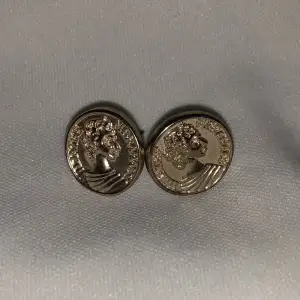 Guldfärgade örhängen som ser ut som små mynt. Har aldrig använt dom. Är ungefär en cm stora. Vikt ca 3g.