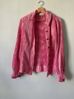 Rosa plisserad skjorta från Ganni - Material: 100% polyester Skick: Denna har ngr tråddragningar (se sista bilden för exempel) men inget man tänker på pga strukturen i plagget.