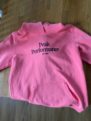 peak performance huvtröja - Säljer denna rosa hoodie från peak performance. Aldrig andvänd pågrund av storleken. Nypris runt 900kr. Dock har tröjan små blåaktiga fläckar. Några stycken på armarna. Hör av dig om du vill ha fler bilder på tröjan!
