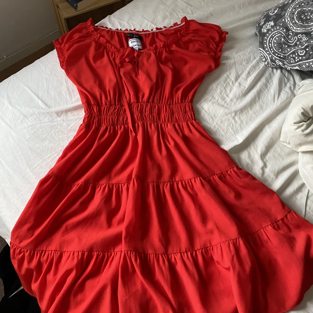 Röd klänning från Daisy Grace med knytning där fram. Aldrig använd så är i nyskick. Den är i storlek xs men passar mig som är  M/L perfekt också eftersom den är så stretchig!. Klänningar.