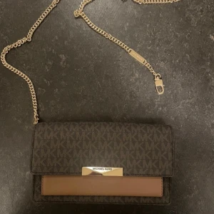 Brun Michael Kors Väska - En rymlig och elegant väska som endast är använd en gång. Den är väldigt rymlig, är perfekt för jobb eller fest osv. Passar bra som plånbok p.g.a dem avtagbara banden.  Dustbag medföljer! Originalpris: 1 556kr. 