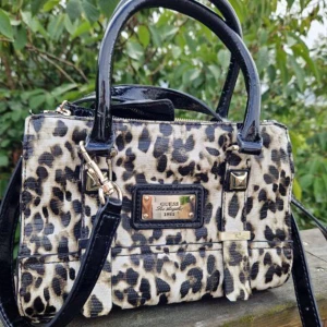 GUESS väska  - Leopardmönstrad snygg väska från GUESS i fint skick. Längd 24cm, höjd 18cm, bredd 9cm. Har både handtag och avtagbar axelrem. 3 innerfack 2 med dragkedja och ett mittenfack med knapp. Nypris cirka 1 100 säljer för 400kr plus frakt.