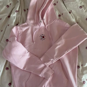 Tommy hilfiger hoodie - Rosa Tommy hilfigerhoodie med snören och munkficka, fått någon konstig fläck från tvättmaskinen som tyvärr inte går bort, fint skick i övrigt!