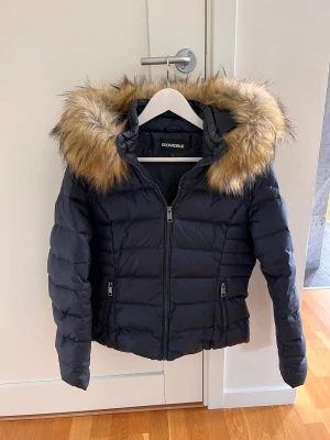 Rock’n Blue mörkblå dunjacka stl 42 - Säljer min sparsamt använda dunjacka från Rock’n Blue i storlek 42. Den går att justera i midjan och pälskragen (fuskpäls) går att ta av. Mycket gott skick.