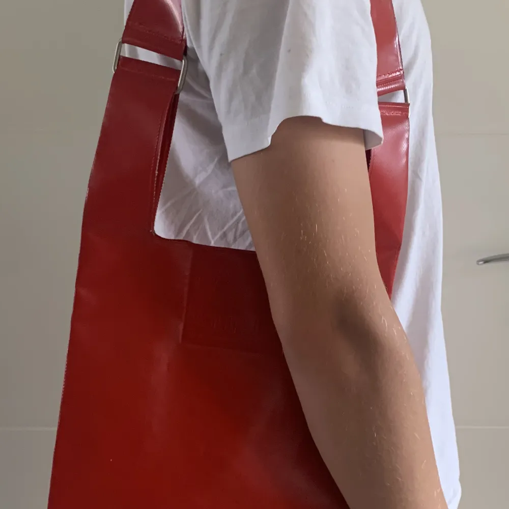 Röd axelväska i plast från Equipaje BCN. Knappt använd, men har fått ett litet märke på axelremmen, se bild. 35x24 cm är själva väskan, förutom remmen.. Väskor.