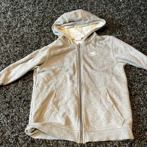 Hej jag säljer den här gråa nike hoodien den har inga skador eller hål zip hoddie är i storlek 147-158 jag säljer den eftersom den är lite för liten pris kan diskuteras vid köp - grå nike zip hoddie 147-158 storlek 