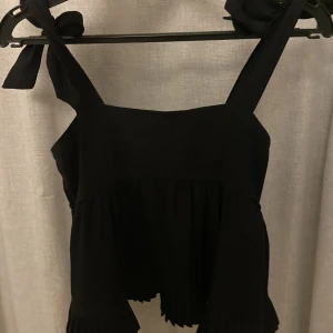 Svart topp - Säljer denna söta toppen med knytning i banden och volang där nere. Köpt på Zalando. Mycket bra skick, inga defekter. Pris kan diskuteras!😇