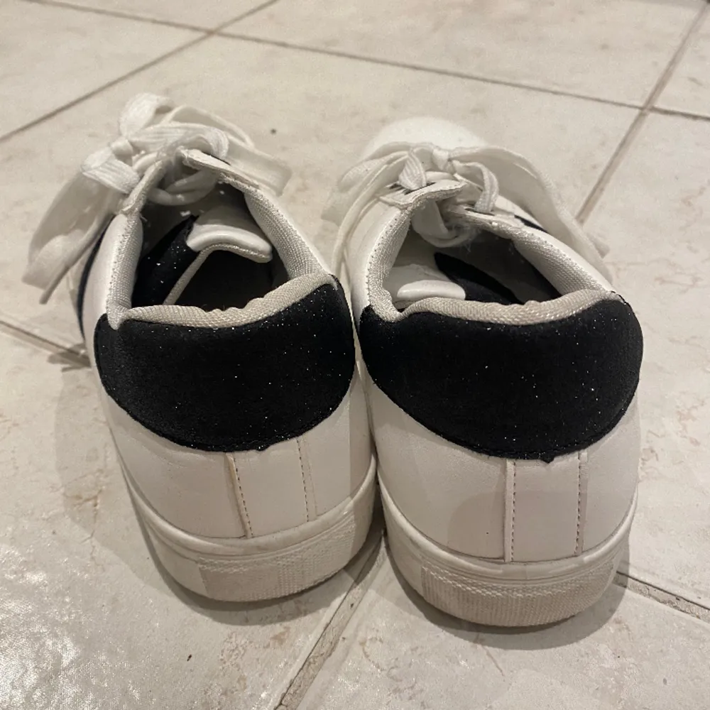 Supersnygga vita sneakers med svarta glittriga detaljer, skorna har endast använts två gånger och är i jättebra skick. Skor.