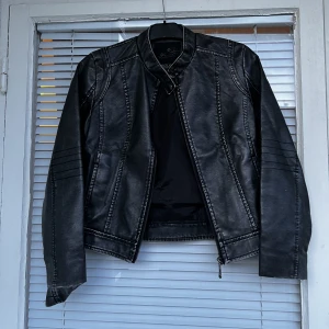 Läderjacka (fejk / vegansk läder) skinnjacka - Läderjacka (vegansk läder) i fint skick säljes. En knapp fattas, se andra bild. Strl: 38-40. Gråsvart färg. 