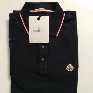 Moncler piké - Säljer nu min nyinköpta moncler piké för att den var lite för liten för mig.  Den är mörkblå. Strl M Priset kan ändras vid snabb affär. Skriv gärna för fler bilder!