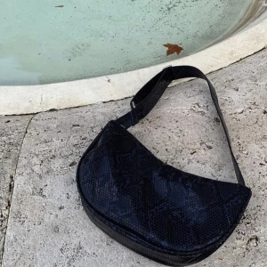 Cross body bag /axelrems Väska bäck södergaard  - Väska från bäck södergaard som går att använda på olika vis. Endast använd en gång. Mörk med reptilliknande material. Nypris 700kr