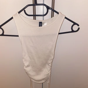 Tajt linne med snören på sidan - Ett tajt linne i storleken Xs från Divided på h&m. Har små fläckar som inte syns så mycket, på bild tre så ser du en blyertsaktig fläck. Det går säkert/förmodligen bort i tvätten med lite fläckborttagning. Annars inget fel🫶 Säljer för att den är för liten