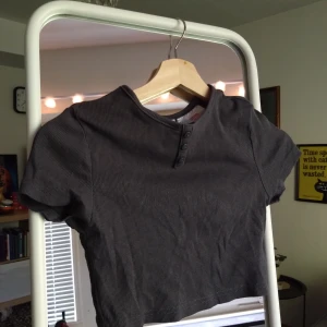 Grey high-neck crop top. - Kortmidjad, svart/grå t-shirt med dekorativa knappar. Skön som pyjamas eller snygg som fit.  Mjuk och skön. Tröjan säljes i mycket gott skick.