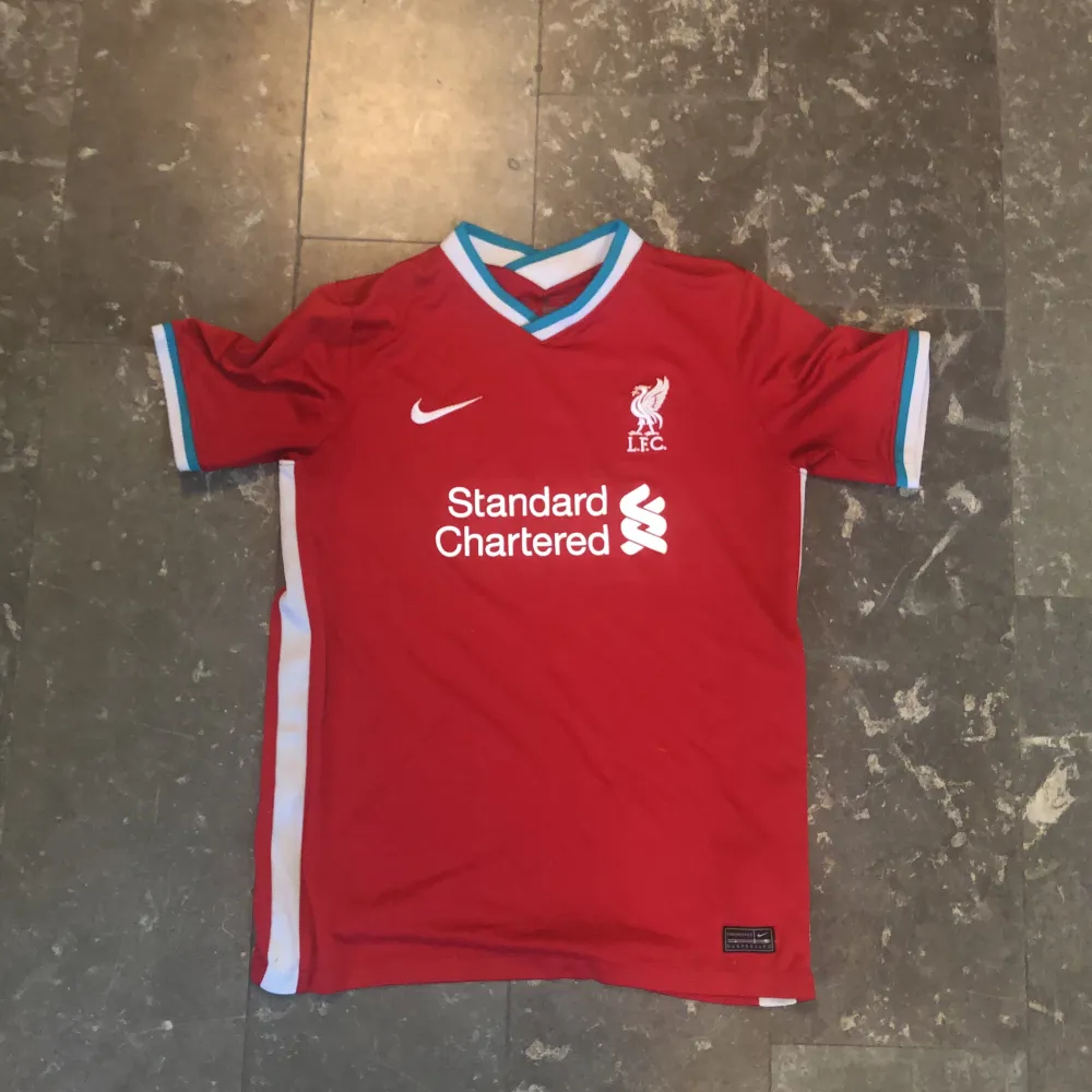 Säljer denna Liverpool Hemma tröja som nu blivit för liten. Köpte den i början utav 20/21 säsongen och är inga fel på. Tröjan sitter stort och om ni har några frågor eller funderingar är det bara att höra av sig👊🏻. T-shirts.