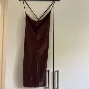 Klänning - En brun klänning i glansigt matreal  som är korsad och lägre i ryggen 
