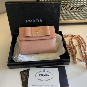 Prada plånbok  - Sälja min gulliga Prada Pink Saffiano Leather Bow Flap Compact Wallet. det är jättefint skick, ingen anmärkning eller slitningar på. Det kommer med original lådan och authenticity kort som är äktighetbevis för plånboken. Priset ink. Frakten 