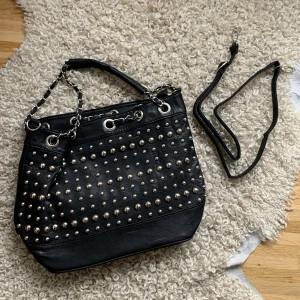 Väska med nitar - Jag säljer denna väskan med nitar pga att den aldrig används! Fint skick!! Ett axelband till väskan följer också med.❤️