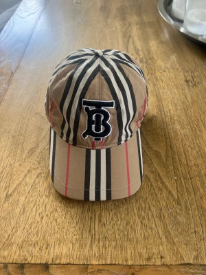 Burberry keps  - Burberry ”BT” logo keps till salu.  Storlek M men går att justera till specifik storlek. 9/10 i skick finns inga tecken på användning.  Fraktas spårbart eller hämtas på plats.