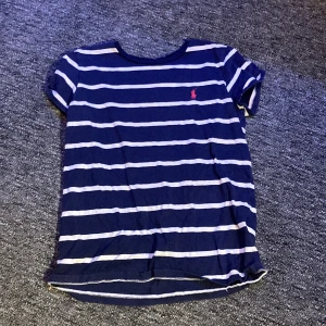 T-shirt - Mörk blå,vit randig t-shirt med en rosa ca 1 1/2 cm rosa ryttare på vänster sida storlek det står it på men mellan 150-156 