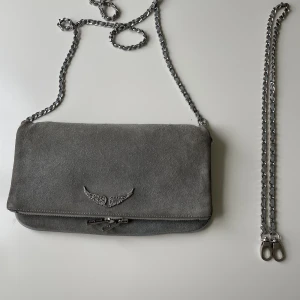 Zadigväska grå mocka - Stor modell i grå mocka. Långa kedjan är som ny. Baksidan har lite missfärgning av blå jeans men inget som stör.