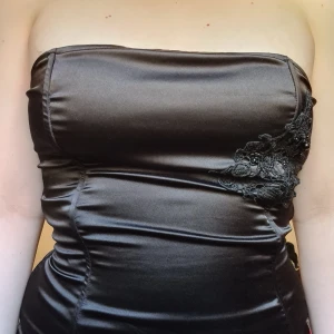 Korsettopp svart med pärlor - Den har "boning" därför ganska strukturerad (kan därför inte vikas i frakten därför lite dyrare än amnars) men tyget ändå töjbarttyg. Går snöra upp, öljetterna sitter lite löst. 