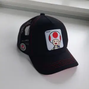 Jag säljer en fin Super Mario Bros Toad 2 Trucker Cap. Den är aldrig använd och är i juniorstorlek. 