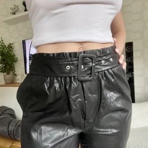 Skinnbyxa - Byxor i fakeskinn. Ena stålringen i skärpet har lossnat, annars inget slitage 