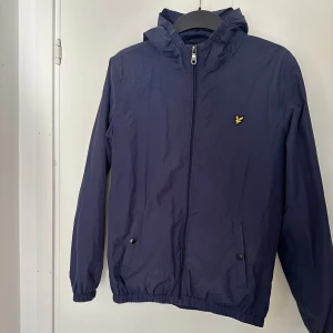 Lyle & Scott vindjacka - En marinblå vindjacka från Lyle & Scott. Finns lite smink vid kragen, men de går att tvätta bort. Köpt på kidsbrandstore. Storlek 14-15år (Längd 164-170cm. Byst 86-88cm. Midja 75-76cm) (Kidsbrandstores storleksguide) Färg: Navy Blazer