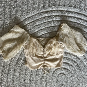 Topp  - En somrig topp som är oanvänd!med spets tyg, blommiga mönster och knyt fram vid magen. Modellen är kort som en magtröja. Den är något stor vid bröstet för mig. I ryggen är det stretch så den anpassas efter kroppsform. Storlek M. Färgen är creme vit. 