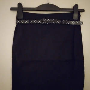 Kort, knälång svart snäv kjol med skärp, från Divided. Helt NY & OANVÄND. Strlk 34, XS. - Kort, knälång svart snäv kjol med prickigt lackat skärp (avtagbart), från Divided. Helt NY & OANVÄND. Strlk 34, XS. Bomull. Tags sitter kvar sedan inköpet. Felfri.