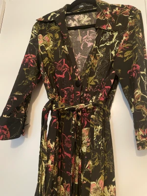 Blommig skjortklänning Zara - Fin blommig klänning från zara. Knappar i fram och bälte i midjan. Går nedan för knät. Strl S men är man M kan man också ha den. 