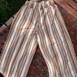 Snörade, vida byxor  - Linjerade byxor med snörning i midjan: trådarna är lite fransade uppe vid midjan och byxorna är väldigt korta. Passar om man har korta ben och vill ha vida byxor. Ca 150cm långa byxor 