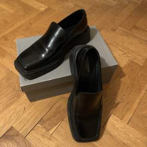 Jättefint skick! Använda en gång. Nypris 1400  Från hemsidan: Eyra är minimalistiska loafers med en uppdaterad design. Modellen är i svart skinn, med skarp fyrkantig tå och dekorativa sömmar på ovandelen. Den robusta yttersulan har en 45 mm grov klack.