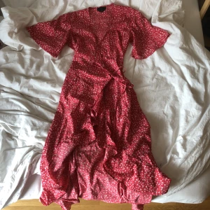 Blommig klänning - Röd omlottklänning med vita blommor på och volang. Storlek xxs men skulle säga att den passar upp till s. Brukar aldrig köpa xxs men den passar mig som brukar ha s.