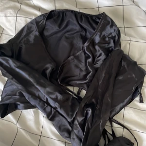Silkes crop top - En svart silkeslen crop top som knyts runt magen med snören som är också silkeslena. Den var för liten för mig så den är oanvänd