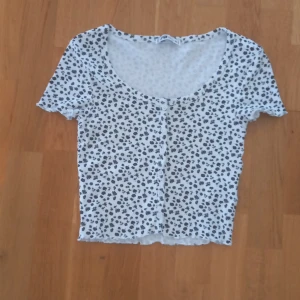 Svart och vit t-shirt - Vit tröja med svarta blommor och vita knappar.