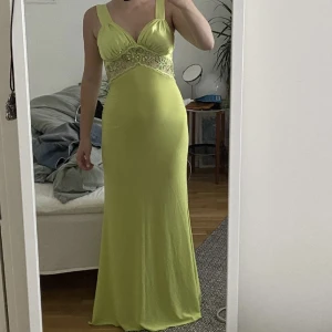 Långklänning med spets - Superfin långklänning i en stark ljusgrön färg med en genomskinlig spetsdetalj under bysten. Spetsen är även dekorerad med små paljetter och sträcker sig runt midjan.