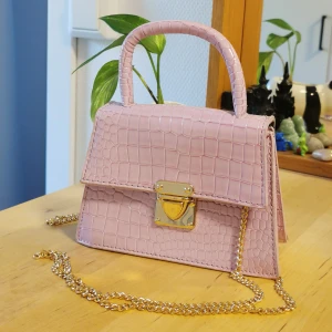 Rosa handväska ormskinn - Liten nätt rosa handväska med ormskinnsimitation. Kedjan kan lätt tas av och sättas på. Köpt på Sellpy. 