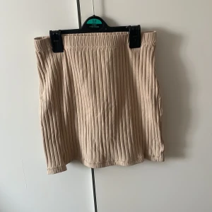 Beige kort kjol - Denna beige korta kjolen med liten slits är köpt från NA-KD i strl. XXS (går även att använda som en topp). Nyskick. Gåva vid köp🍬🍬
